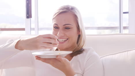 Blonde-Frau-Lächelt-Und-Isst-Einen-Kuchen-Auf-Einem-Sofa