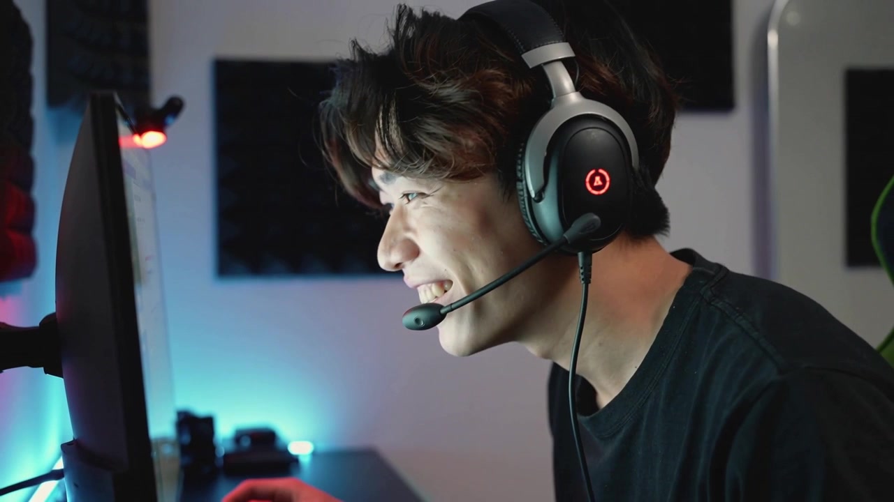Reacting Asian man adjusting mic at home desk to screen alert, wearing dark tee headset, clicking