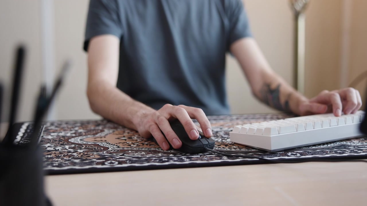 Wide shot Arms And Hands Typing On Keyboard, Patterned Mat Visible, Monitor Edge In Frame, Tattooed Wrist. Media