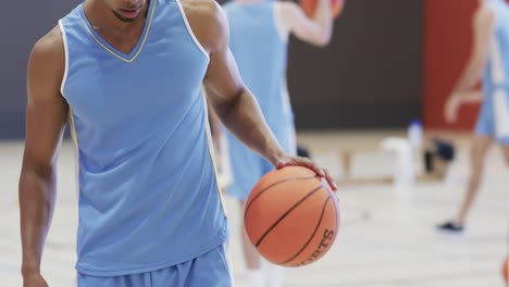 Jugador-De-Baloncesto-Masculino-Birracial-Con-Pelota-Durante-El-Entrenamiento-Del-Equipo-En-Cancha-Cubierta,-En-Cámara-Lenta