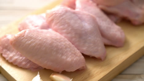 Alas de pollo crudo fresco sobre tabla de madera con ingredientes