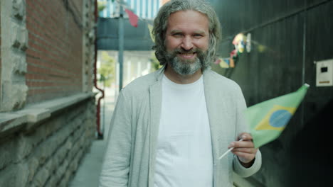 smiling man holding brazilian flag in city alley