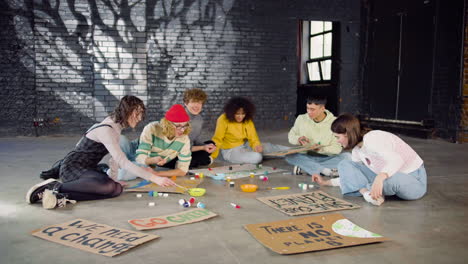 Young-environmental-activists-painting-placards-sitting-on-the-floor