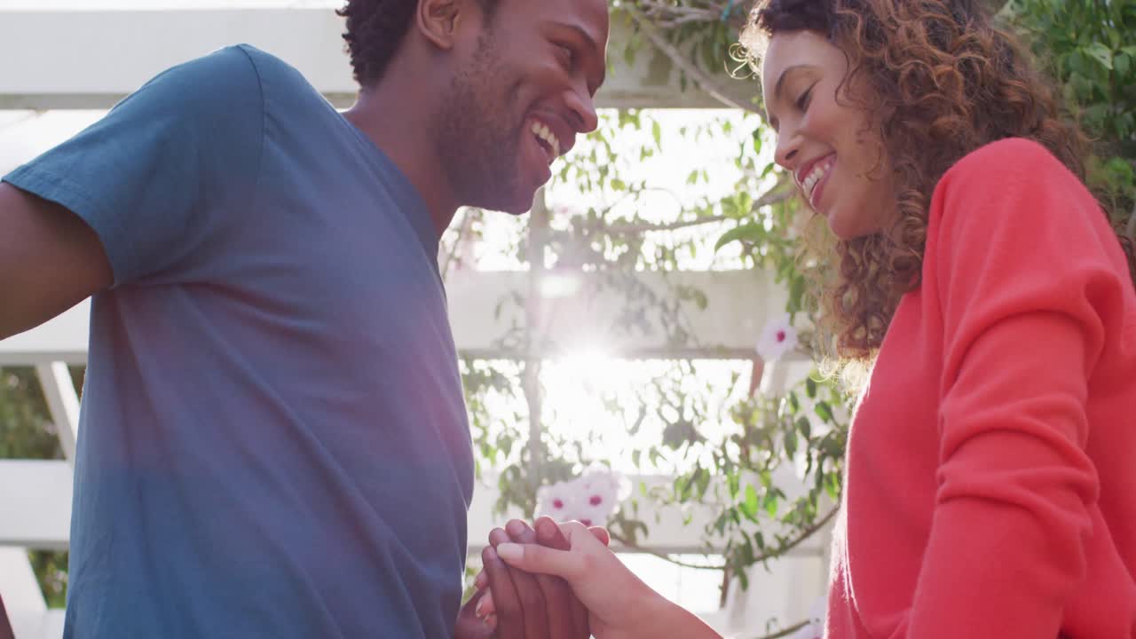 Midsection of happy biracial man proposing to biracial woman with ring