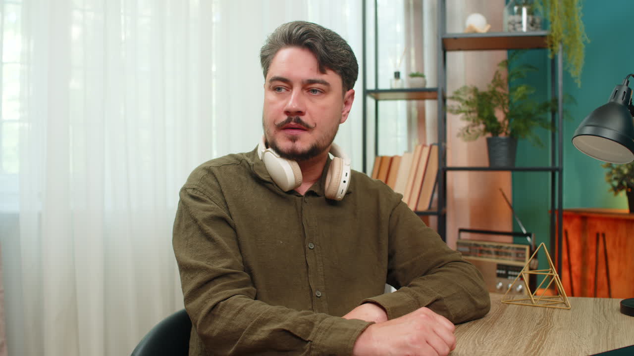 Middleaged man lifts headphones sighs sad after bad audio news feeling disappointed at table desk