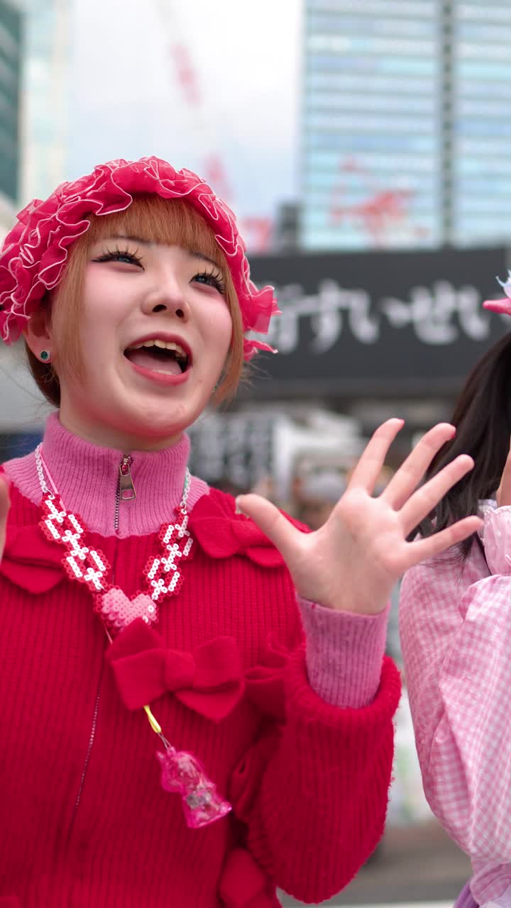 Due donne giapponesi che indossano vivaci abiti decora rosa e rossi ballano con gioia a Shibuya.