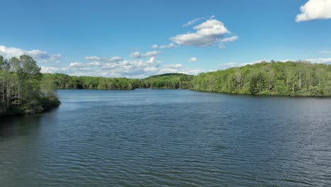 drone shot of peaceful mill creek lake in virginia during sunny day in spring. blue sky and green trees of forest. wide shot.
