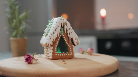 beautiful gingerbread house with intricate icing and green bead decorations sits on wooden tray, soft candlelight, potted plant, cookies, and golden beads