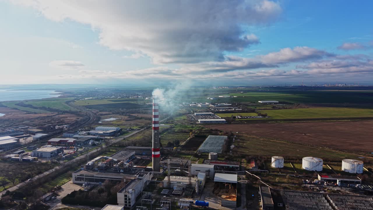 Industrial site with factory, smoke, and green fields in the background