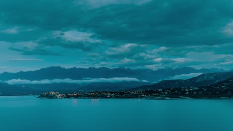 Encender-Las-Luces-De-La-Ciudad-En-Calvi---Córcega,-Después-De-La-Puesta-Del-Sol-Timelapse-Con-Montañas-En-El-Fondo