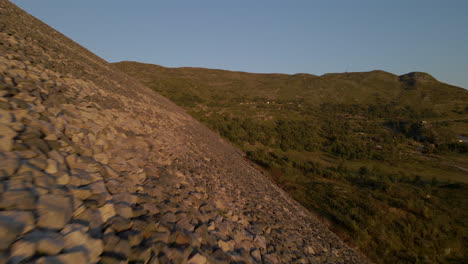 Gliding-aerial-shot-of-Sysen-Dam-rocky-wall,-Hordaland-county,-Norway