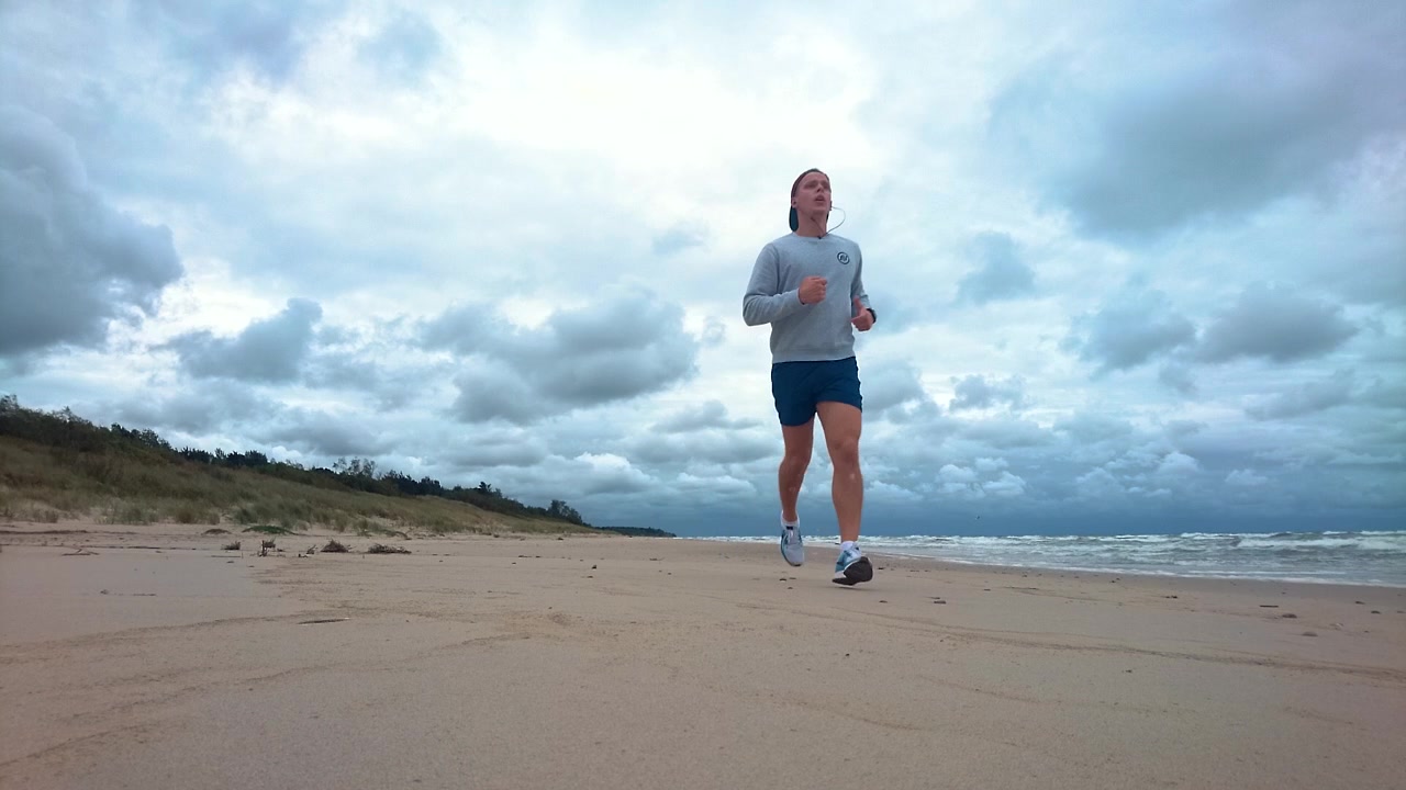 Man is running in the beach in the morning. Windy morning, wavy sea, blue water, cloudy, near storm. Man is in good shape.