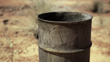 rusty metal barrel located in a dry desert landscape under bright sunlight