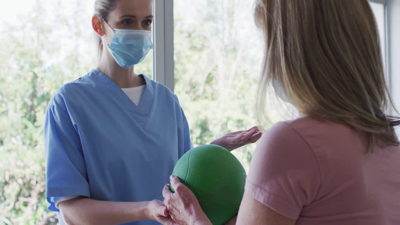 trabajadora de la salud que ayuda a una anciana a hacer ejercicio con pelota en casa