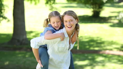 happy little girl getting a piggy back from mother in the park