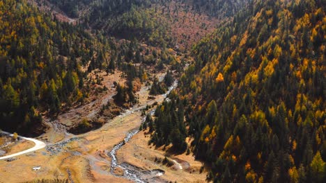 Yellow-trees-dot-conifer-forests-as-river-winds-below-Sichuan-Xingduqiao-Jiagenba-fairyland-mountains,-aerial-establish