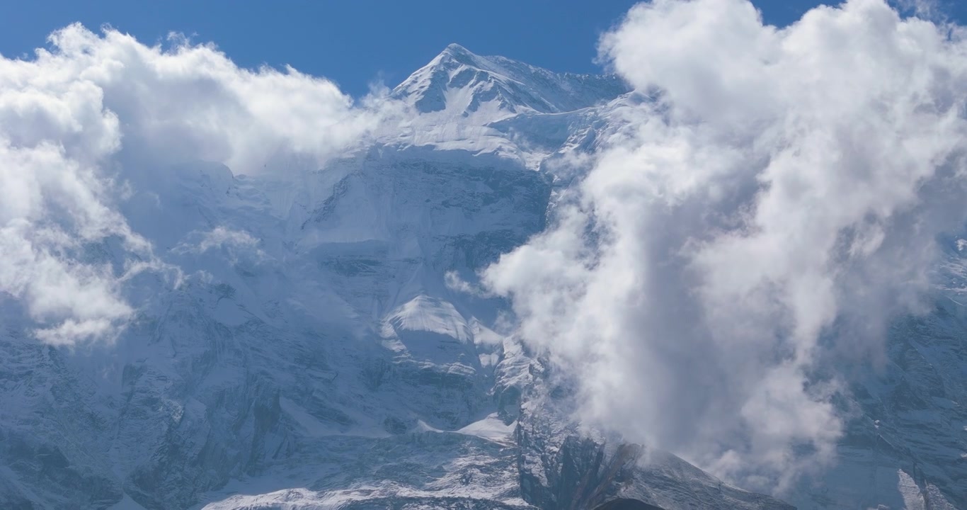 Annapurna Circuit, Manang, Nepal, droneoptagelse af den massive sneklædte side af Annapurna II-toppen, der skaber det visuelle Yeti-ansigt, omgivet af skyer og blå himmel