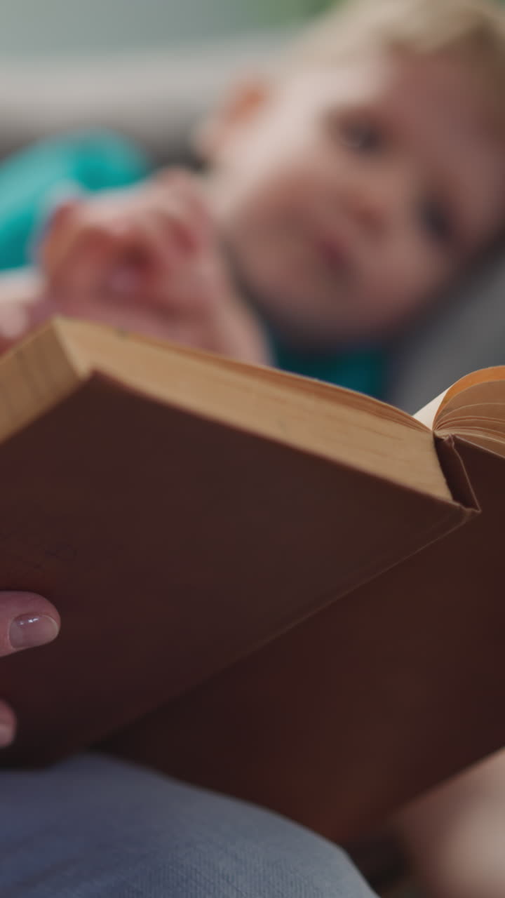 Vintage fairy tales book read by senior lady babysitter to little boy lying on sofa closeup. Grandmother calms down toddler boy for sleeping. Family lifestyle