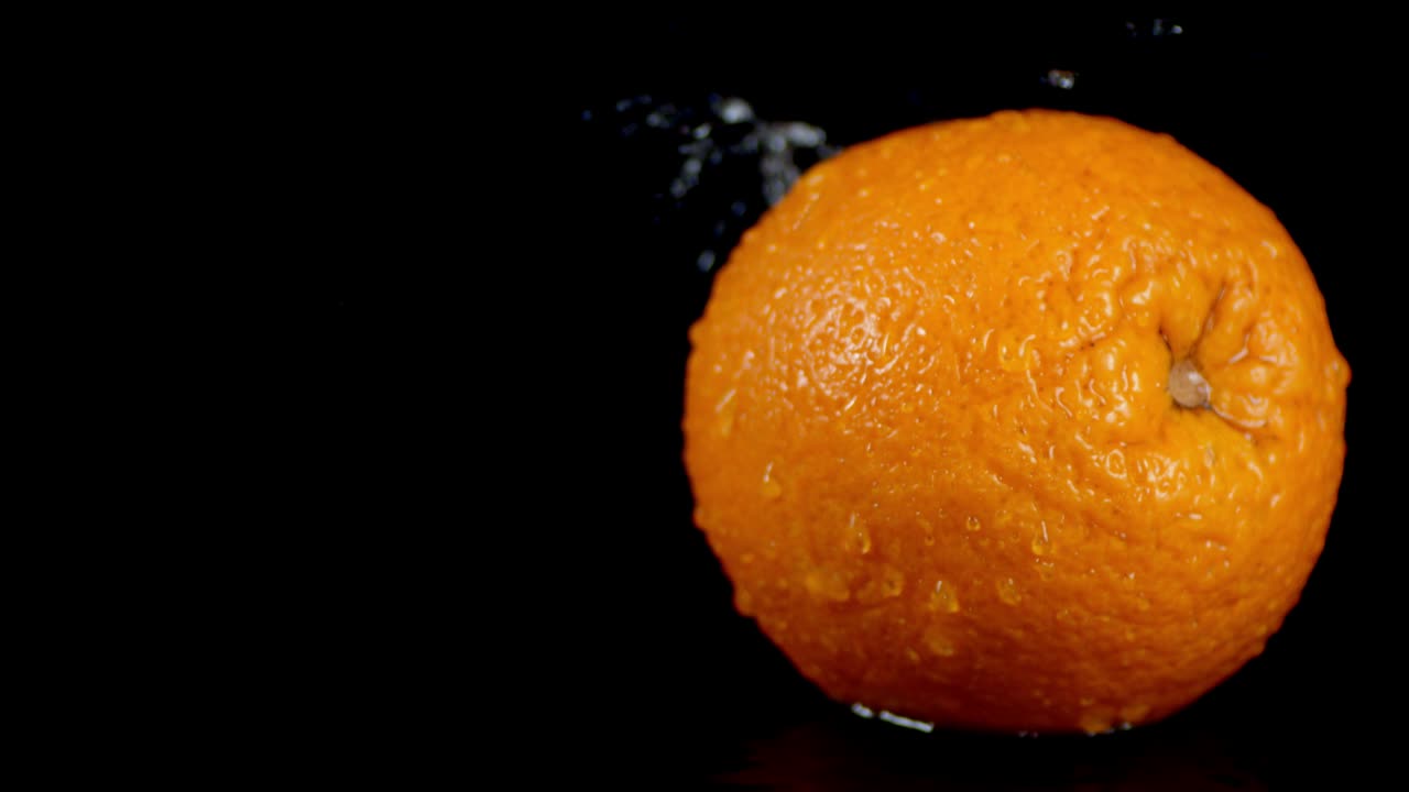 en una sola naranja caen gotas de agua con un salto.