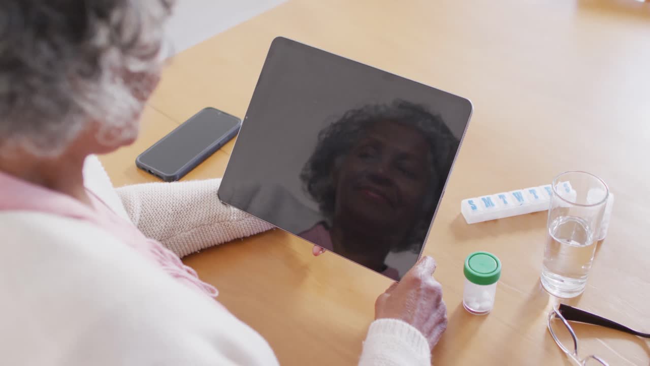 Porträt einer glücklichen älteren afroamerikanischen Frau, die am Tisch sitzt und ein Tablet mit Freiraum für Text benutzt.