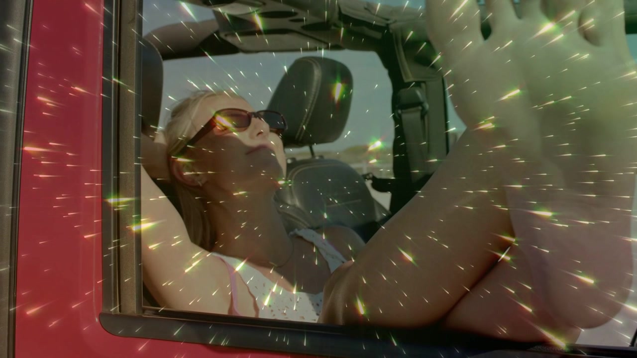 Mujer reclinada en un descapotable rojo, un destello de viaje comienza a extenderse, con los pies apoyados, tomando el sol.
