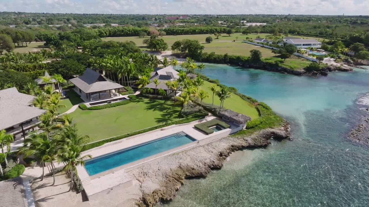 Beachfront villa with lush gardens, long infinity pool, palm trees overlooking turquoise waters in La Romana, Dominican Republic, perfect for travel and real estate visuals