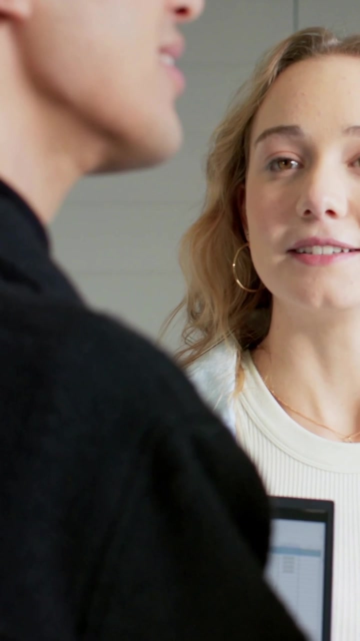 Video verticale: Donna che parla sulla destra, con giacca leggera, alla reception, mentre controlla il laptop, con spazio per il testo.