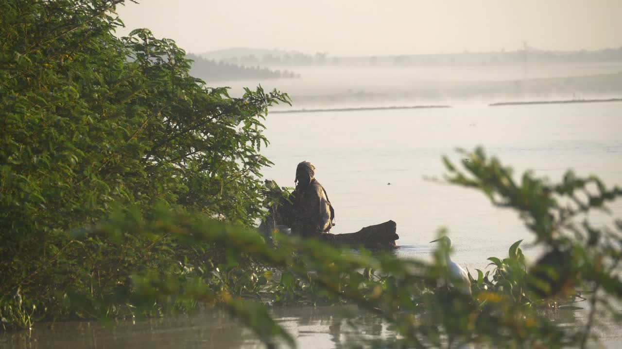An African man on a small makeshift raft casting his net to catch fish in Lake Victoria in Africa.