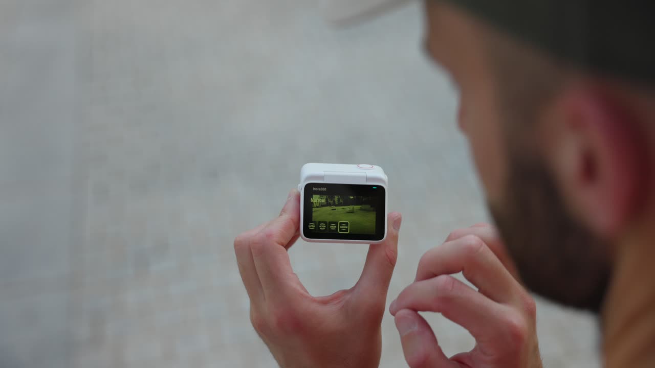 sobre la vista del hombro del freelancer sosteniendo insta360 go 3 action pod sostenido y desplazándose a lo largo de la pantalla trasera con el dedo