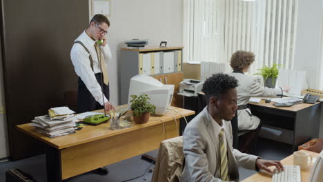 caucasian businessman working stading near his desk and talking on the phone in a vintage office.