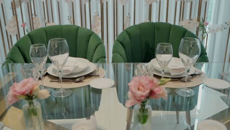 elegantly set dining table with glassware, plates, and pink flowers, featuring green chairs