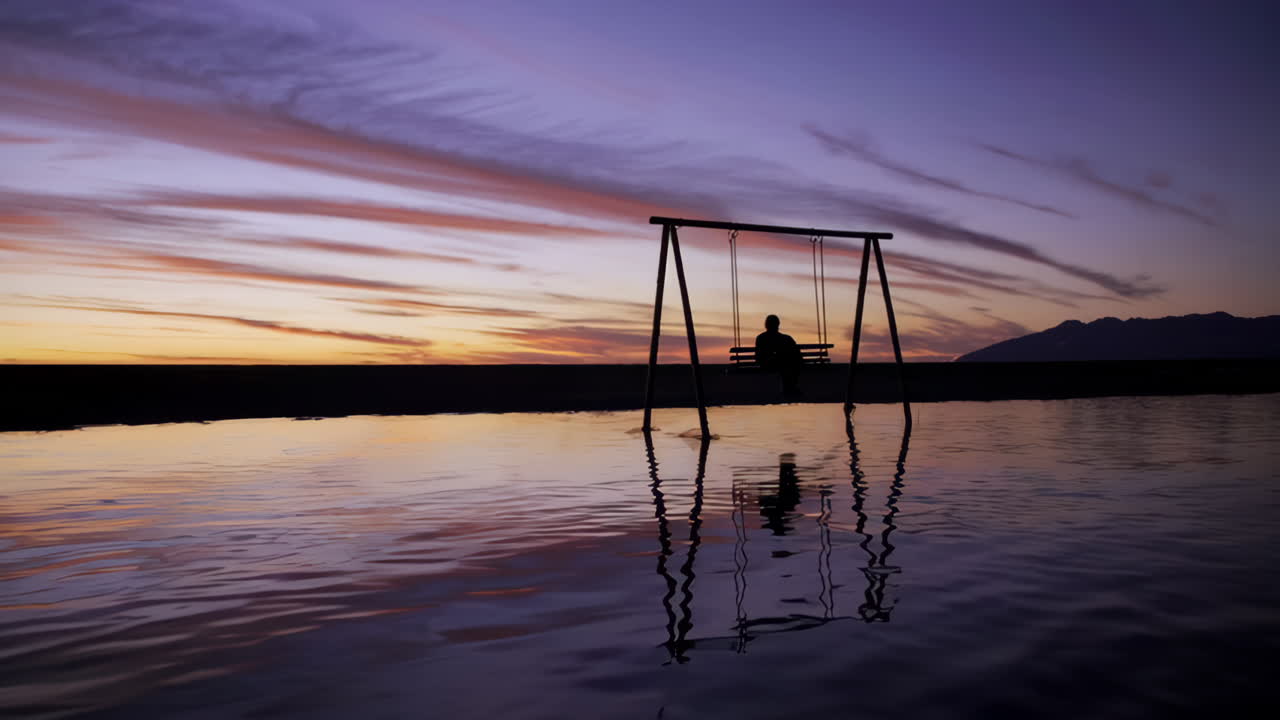 Person on a swing at sunset reflected in water