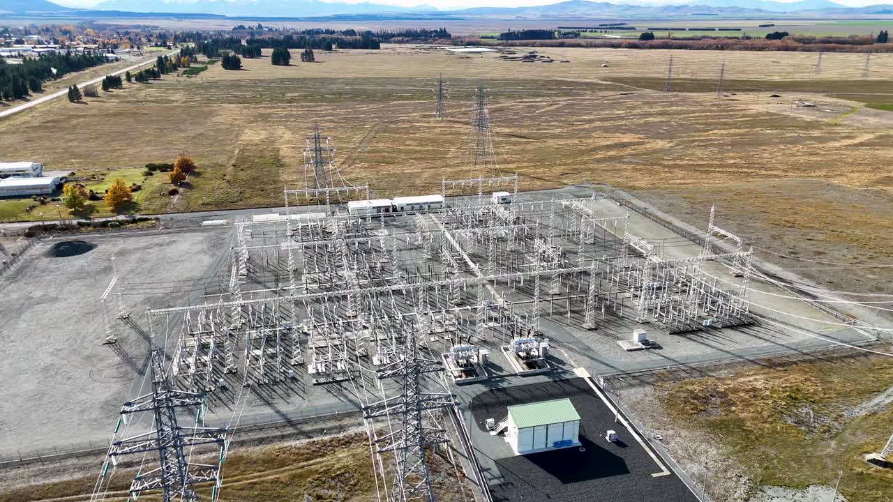 Drone footage captures a high-voltage power substation amidst autumn landscapes at Lake Tekapo, showcasing infrastructure and transmission lines