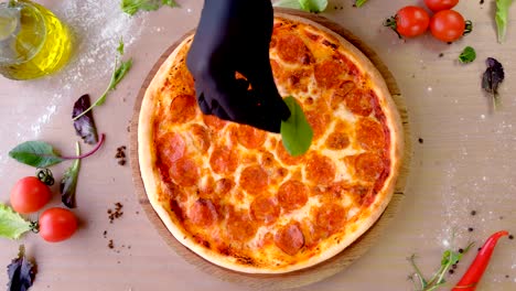 cook puts spinach leaves on pizza salami hands in rubber gloves.