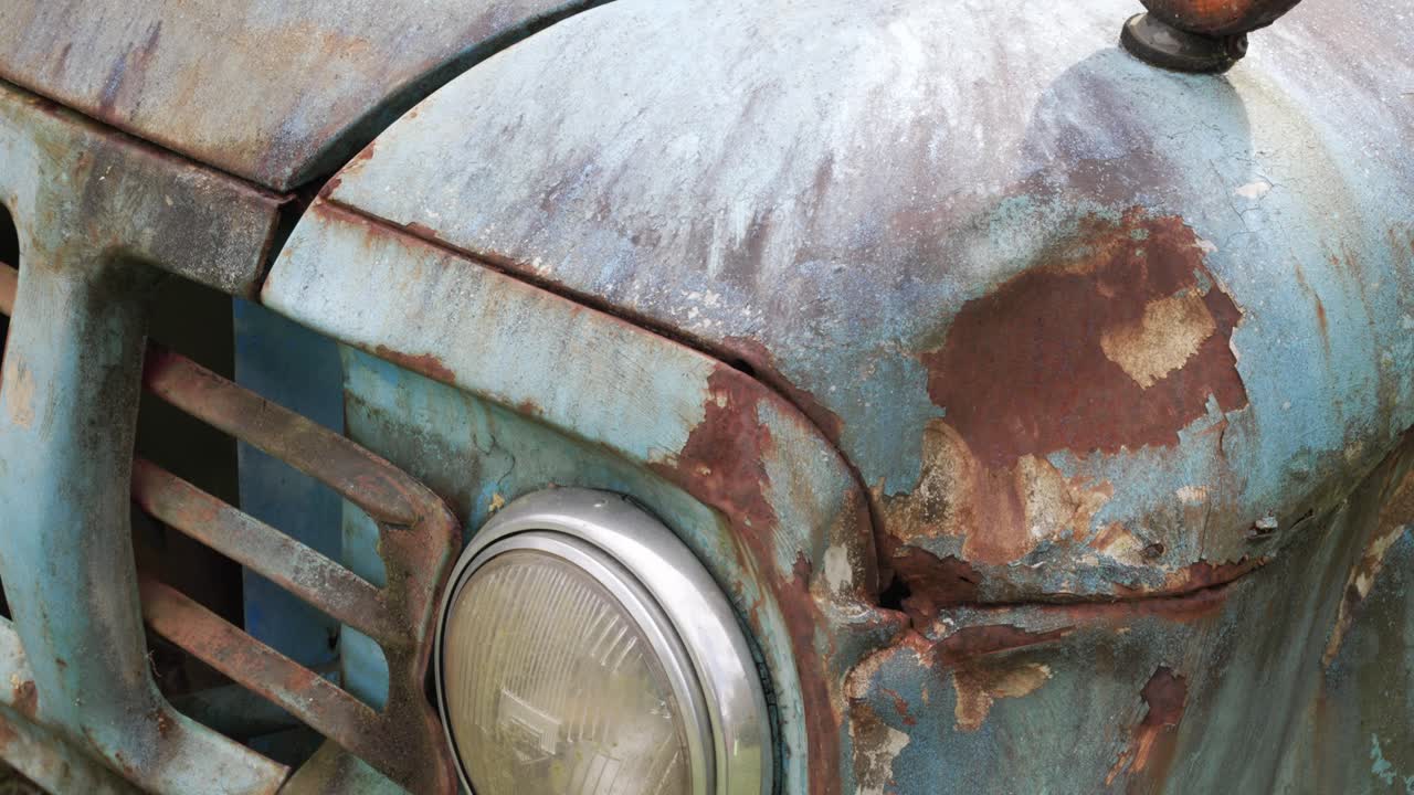 Close up of a rusty headlight on an old, weathered blue truck