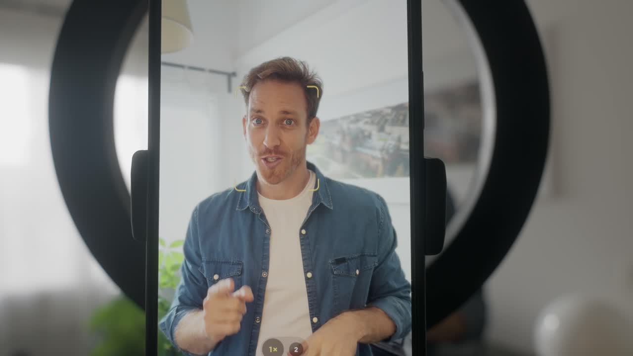 Influencer or social media content creator talking to smart phone camera on tripod or light stand with ring light in apartment or home studio. Recording filming reel live streaming to fans on channel