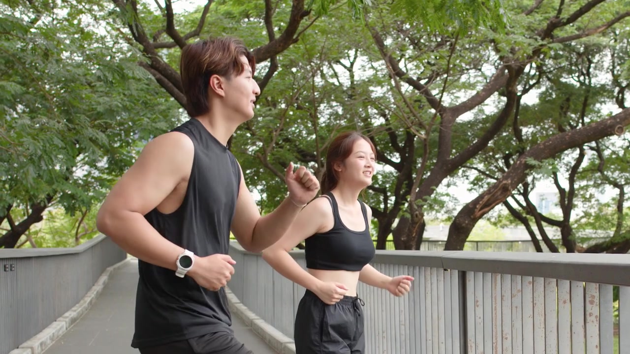 一对穿着黑色运动服的年轻泰国男女在公园的桥上户外锻炼。