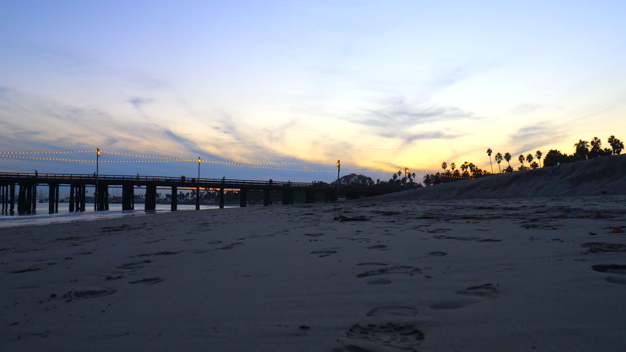 Muelle Stearns Wharf al atardecer con gente caminando por el paseo marítimo, visto desde la playa de arena en Santa Bárbara, California.