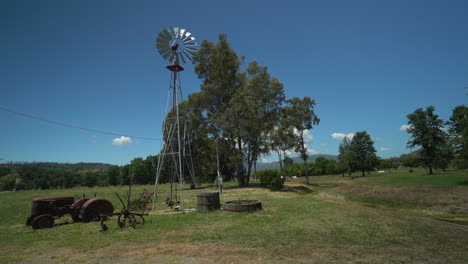 cámara lenta a la derecha de un molino de viento en un rancho rural con un viejo tractor antiguo en primer plano en el norte de california