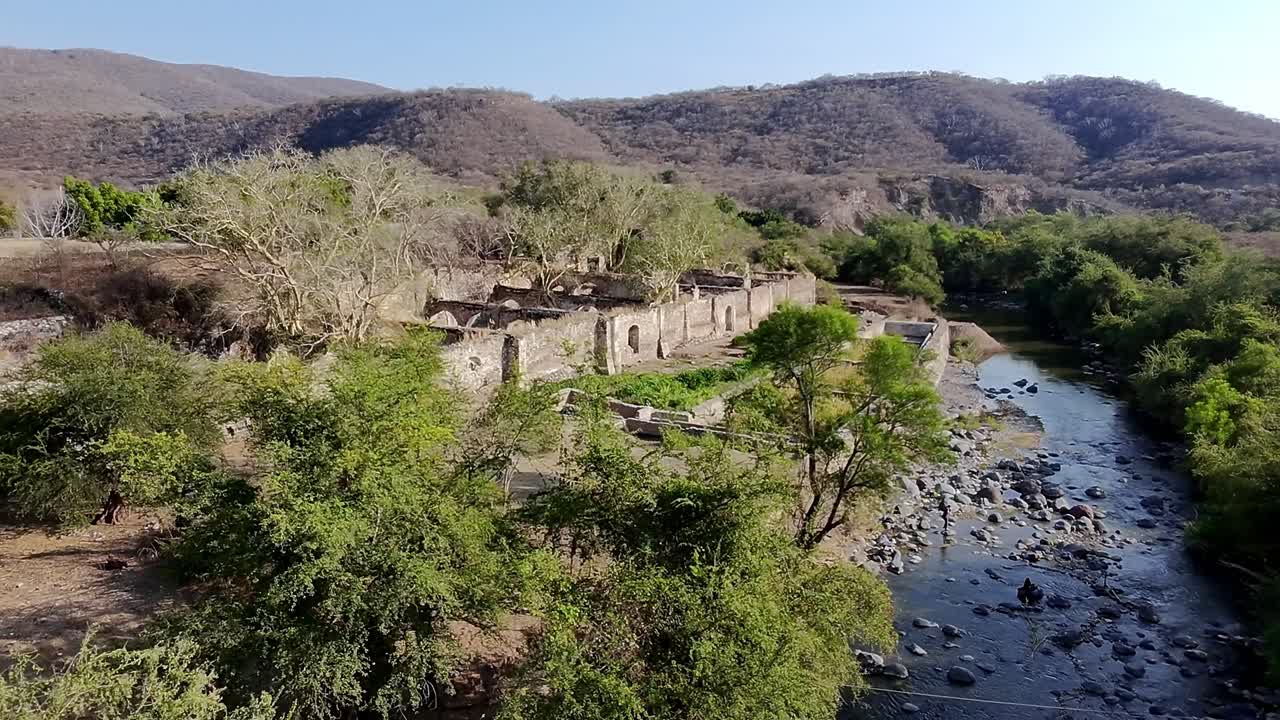 Lush vegetation surrounds the ruins of Hacienda de San Jacinto Ixtoluca in Morelos, Mexico, with a river flowing nearby, showcasing a blend of nature and history