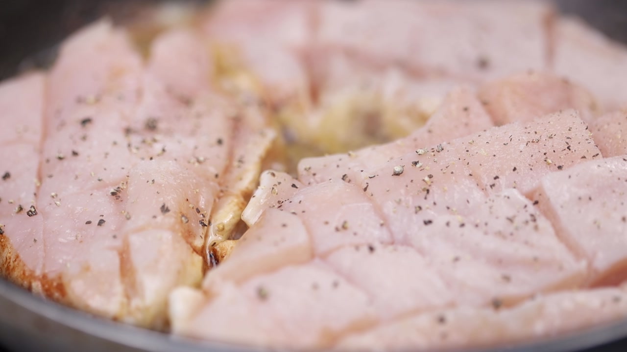 Close up of seasoning chicken pieces with pepper while cooking in pan with visible browning