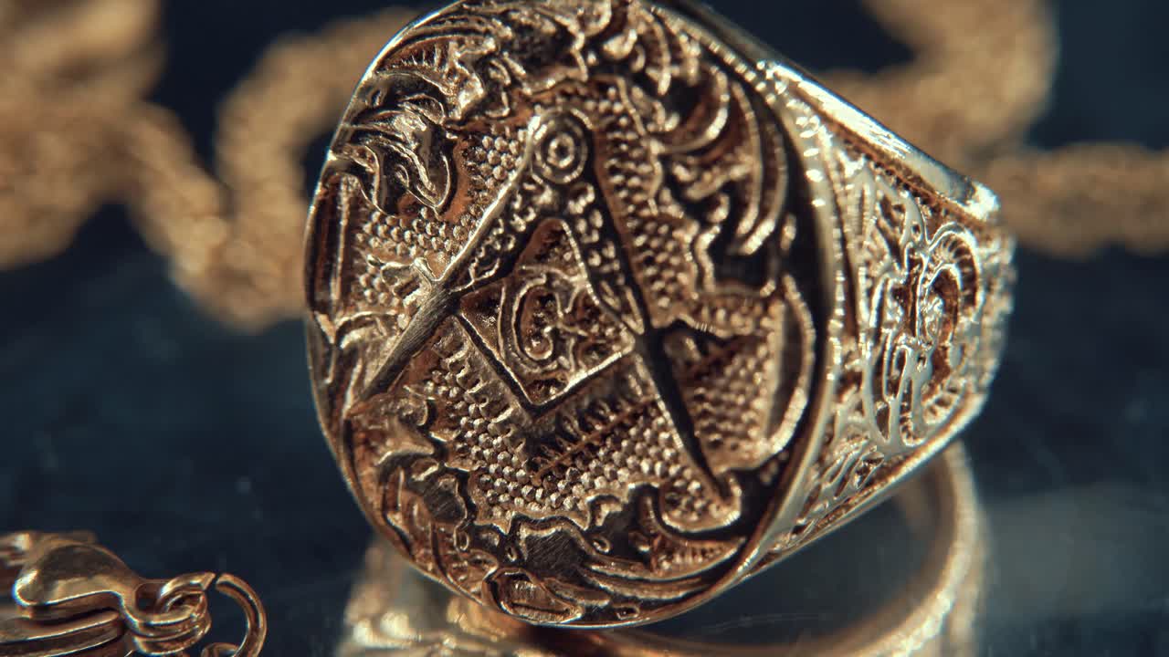 A macro reveal shot of a golden textured freemasons ring, on a rotating mirror stand, illuminati symbol, studio light, 4K video, tilt up movement, necklace shallow depth of field