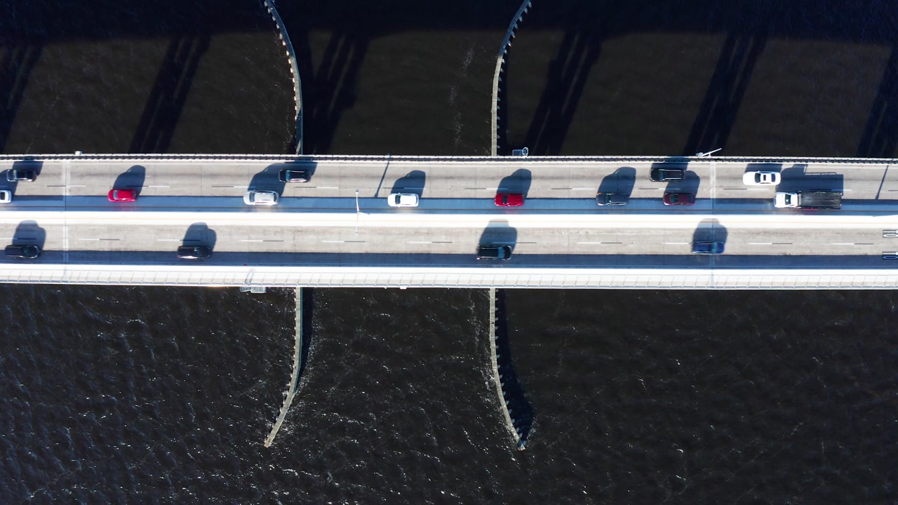 Vehicles travel across a bridge in Fort Myers, casting shadows over the dark water below. Ideal for transportation or city infrastructure themes.
