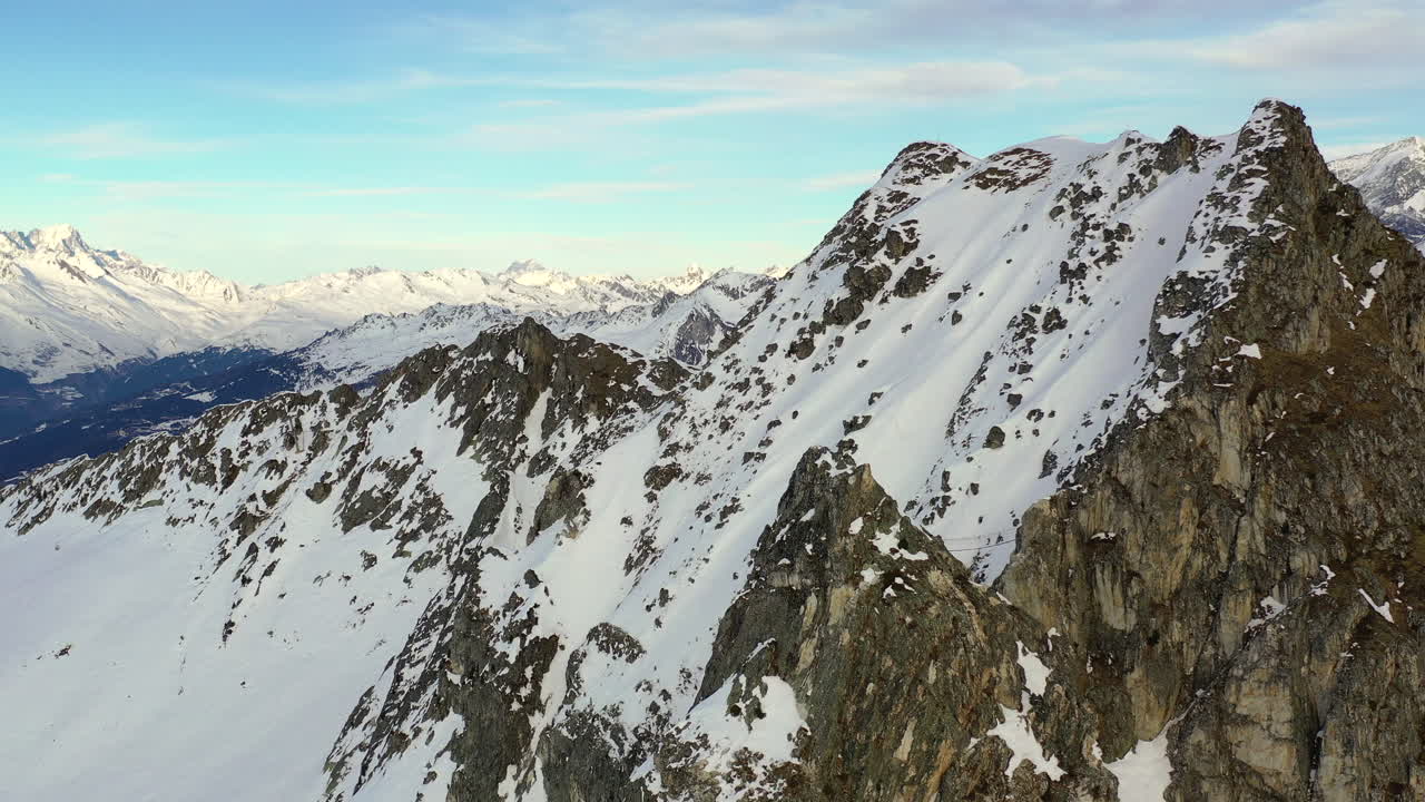 Riprese aeree con carrello in avanti verso una montagna rocciosa coperta di neve, prima di una panoramica a sinistra per rivelare il Monte Bianco, a La Plagne, Francia.