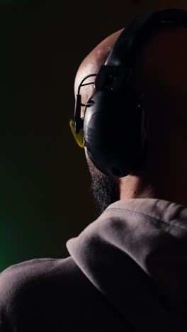 vertical video man in firing range training with rifle, wearing earmuffs to protect hearing