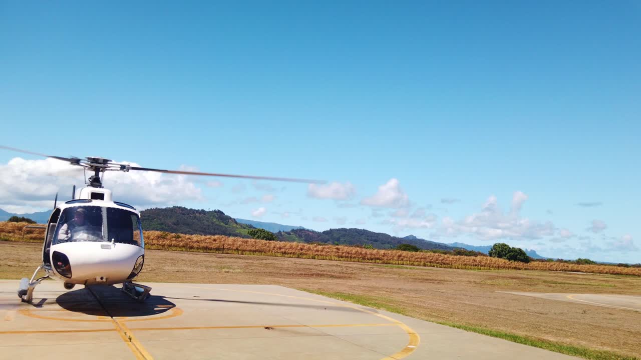 Gimbal wide panning shot of a helicopter getting ready to spin up and takeoff at a heliport on the Hawaiian island of Kaua'i