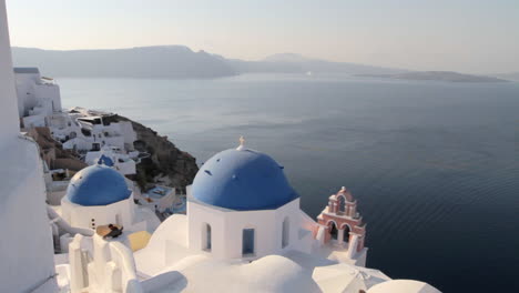 Vista-Pintoresca-De-Las-Cúpulas-Azules-De-La-Iglesia-En-Oia-Santorini-Con-Vistas-Al-Majestuoso-Paisaje-Marino-De-Santorini