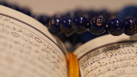 Close up footage of a Quran and a prayer beads near it, the shot is moving in a half circle