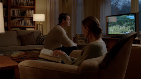 a couple relaxing in their living room, with one person watching tv and the other reading a book