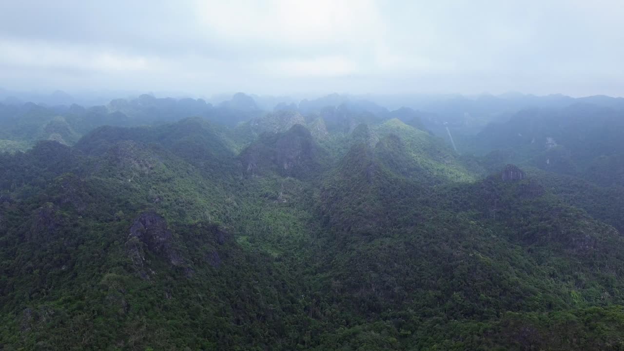 Aerial view slowly pans left across jungle-covered mountains under cloudy daylight